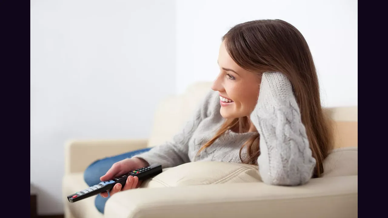 A woman relaxing on a sofa watching television with a remote